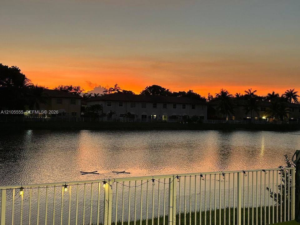 Waterfront property featuring a pond, a metal perimeter fence, and a sunset backdrop
