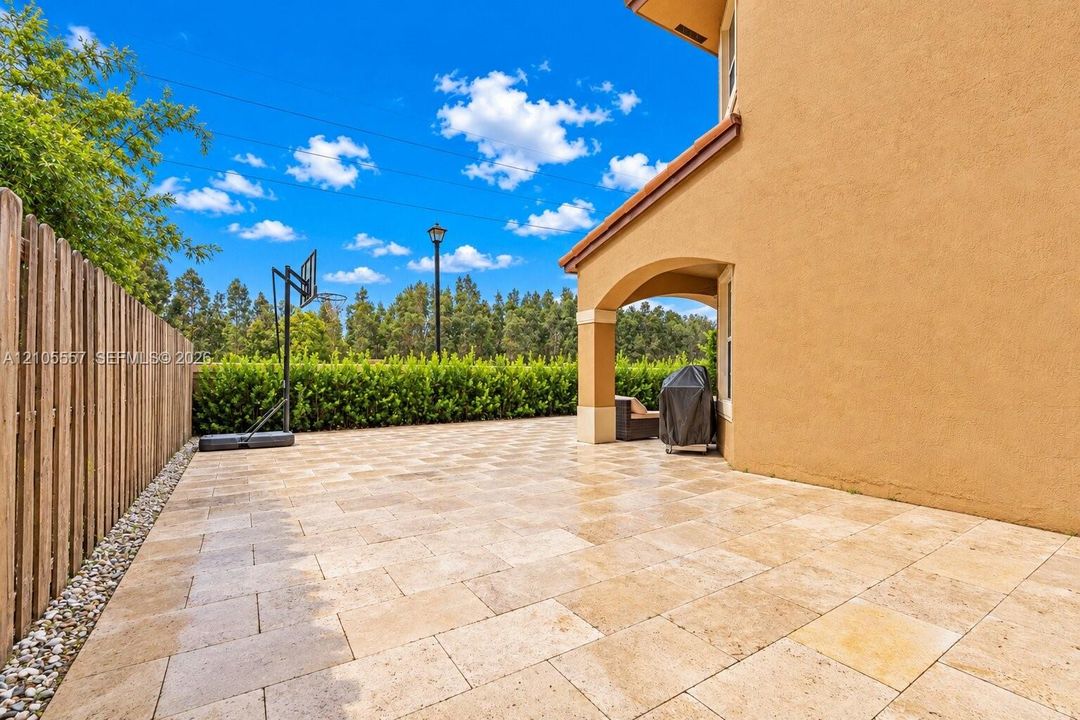 Expansive paver patio with a stucco exterior, an arched covered patio, a privacy fence, and mature perimeter landscaping