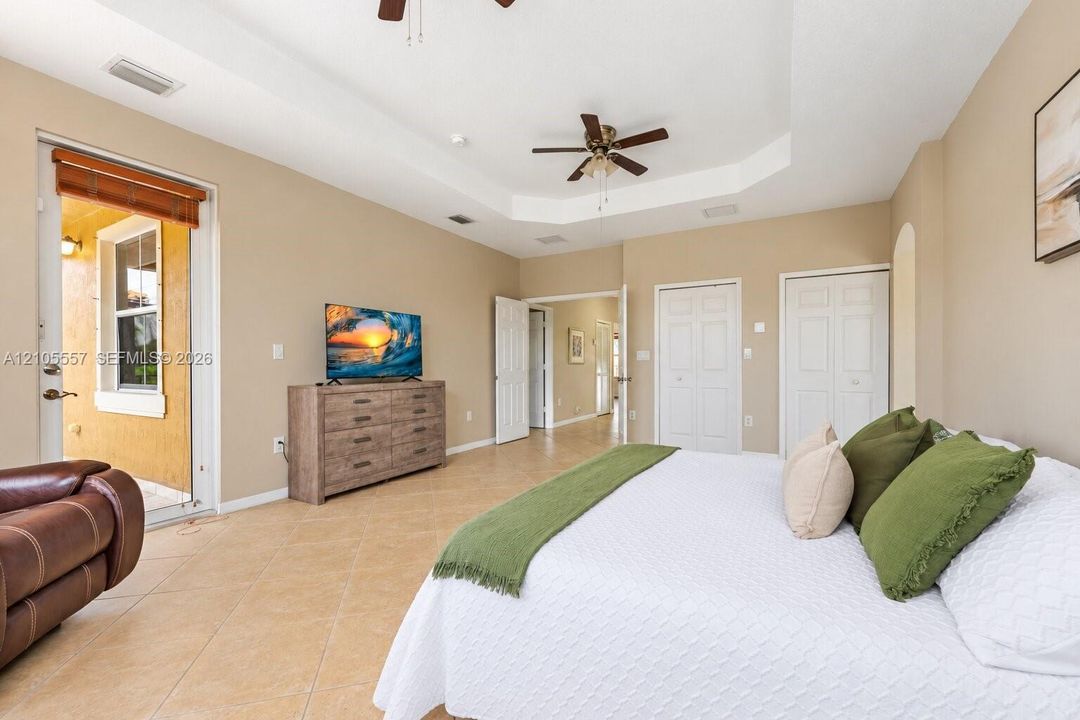 Tray ceiling with a ceiling fan, light tile flooring, and direct access to an exterior patio