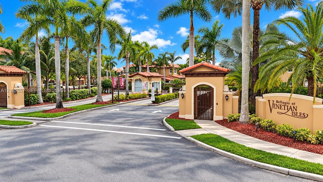 Gated community entrance with a decorative sign, mature palm trees, and manicured landscaping