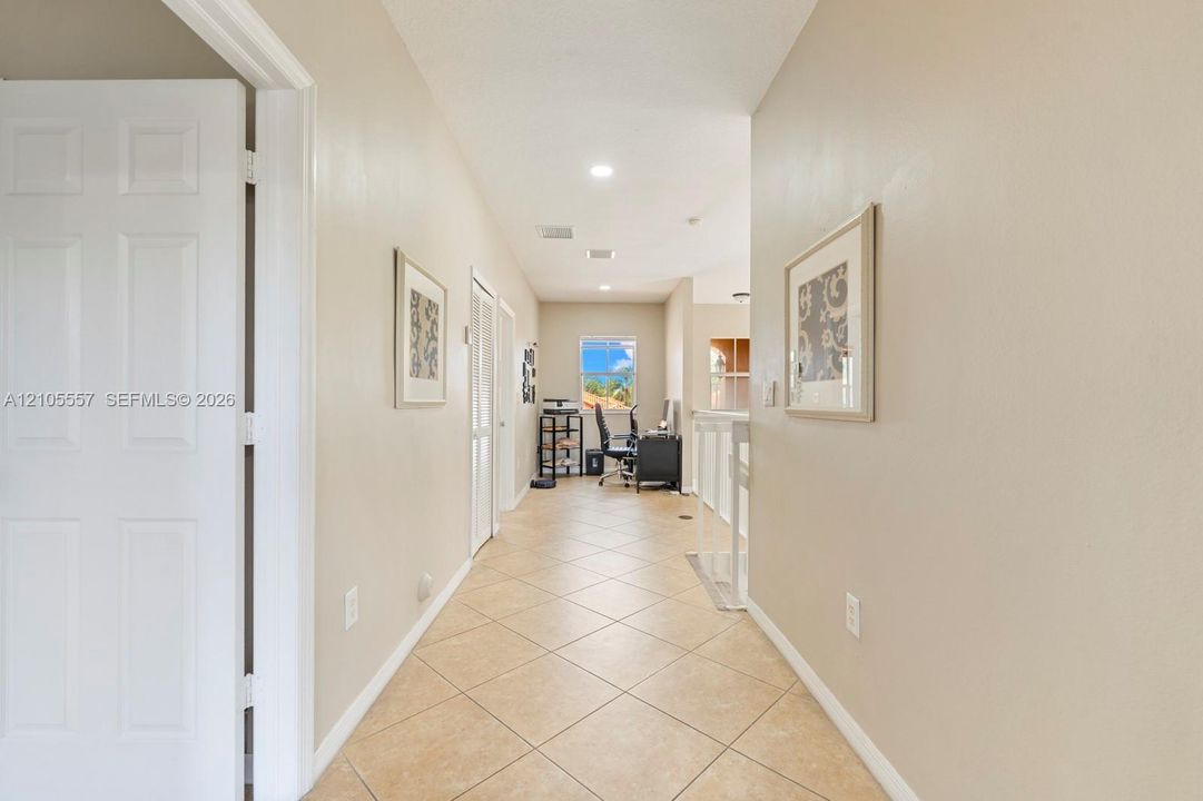 Long hallway featuring light-toned tile flooring, recessed lighting, and a window with visible scenery