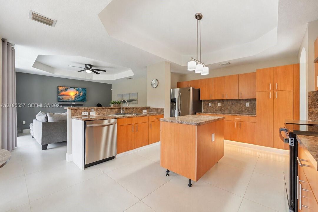 Open-concept kitchen with light wood-finish cabinetry, stone countertops, and stainless steel appliances