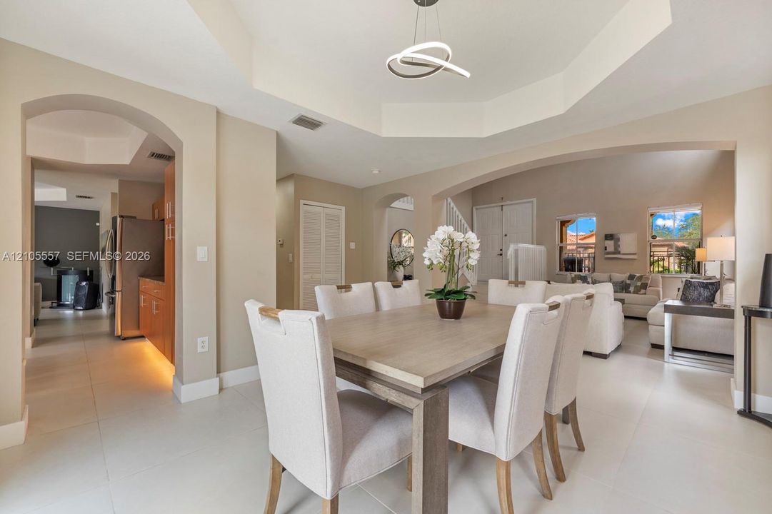 Tray ceiling with a contemporary pendant light fixture, arched doorways, and tile flooring