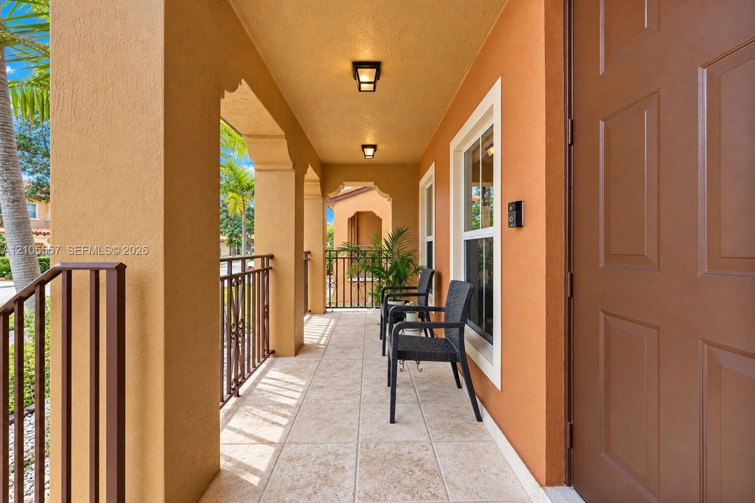 Covered entry porch featuring archways, tile flooring, and dark brown railings