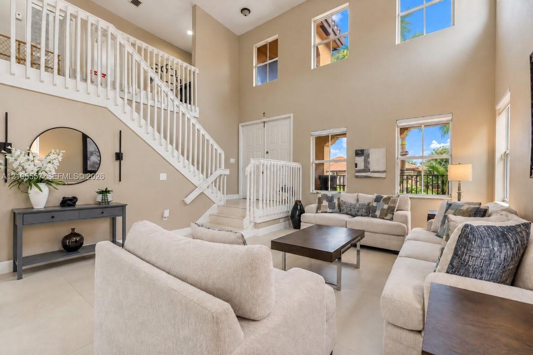 Two-story living area with high ceilings, multiple windows, and a staircase featuring white balusters and handrails