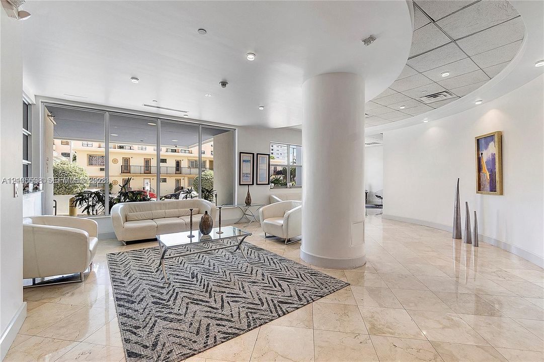 Expansive interior space featuring large format stone tile flooring, recessed lighting, a curved architectural column, and extensive glass paneling