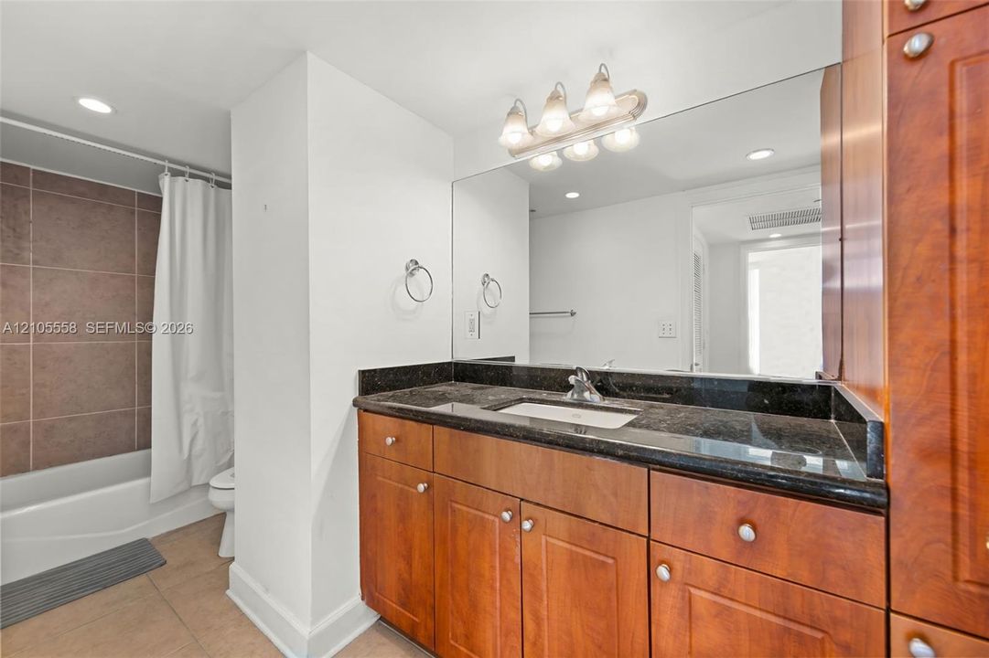 Vanity with a dark countertop and undermount sink, overhead vanity lighting, and wall-mounted mirror