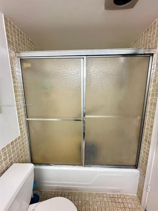 Bathtub with sliding shower doors, textured glass panels, and chrome framing