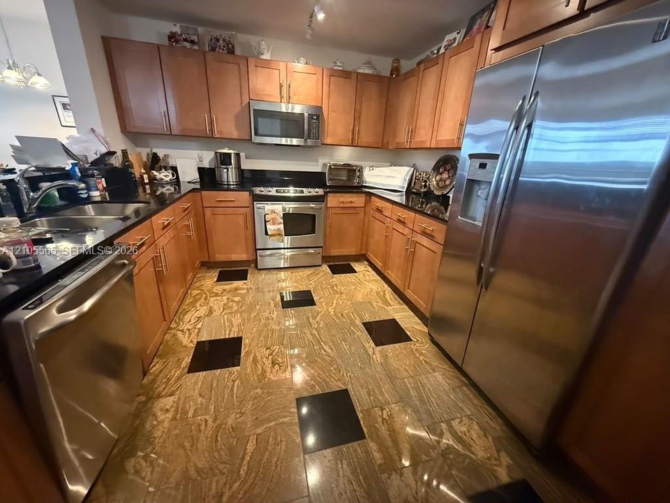 Kitchen featuring natural wood cabinetry, polished stone countertops, stainless steel appliances, and patterned tile flooring
