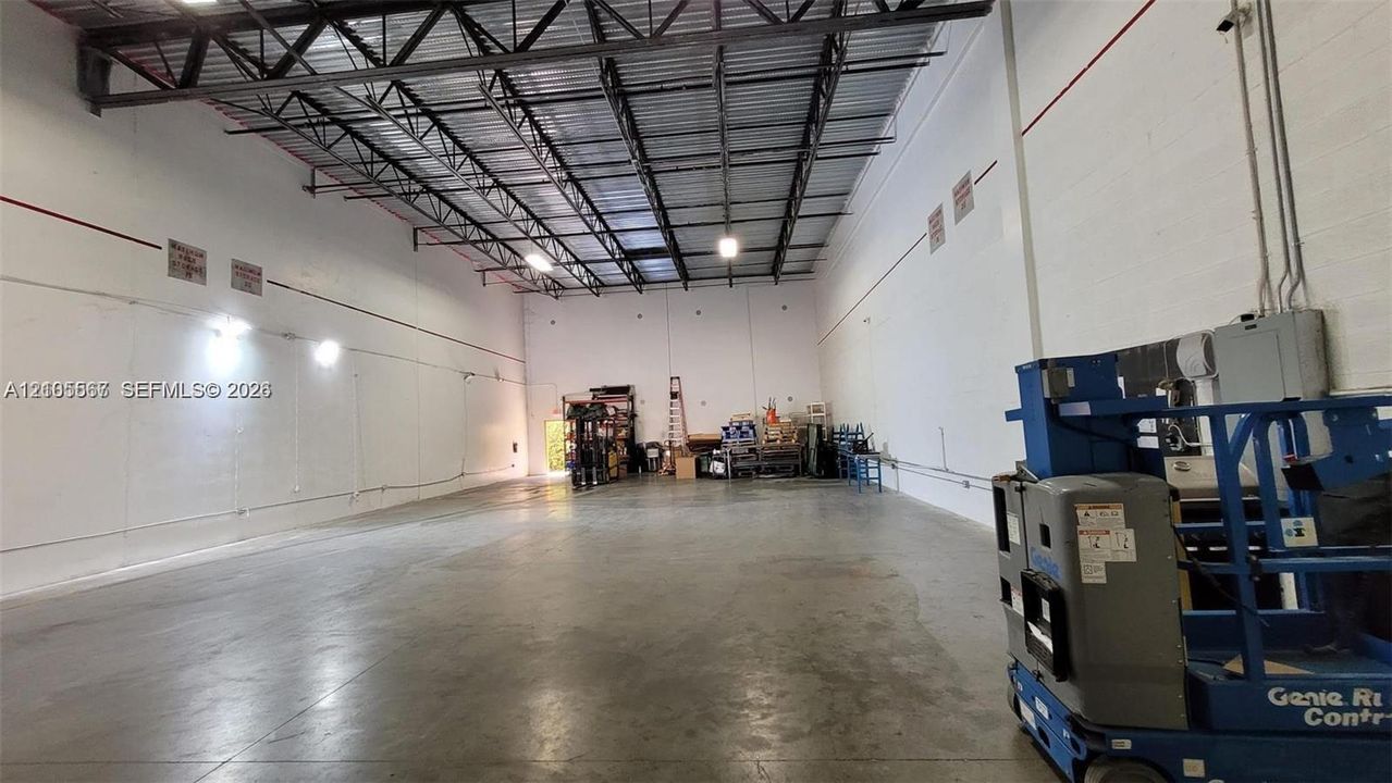 Spacious interior featuring a concrete floor, high exposed metal beam ceiling, white walls, and industrial lighting fixtures