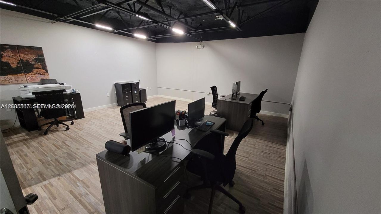 Spacious room featuring wood-finish flooring, white walls, and a black exposed ceiling with track lighting