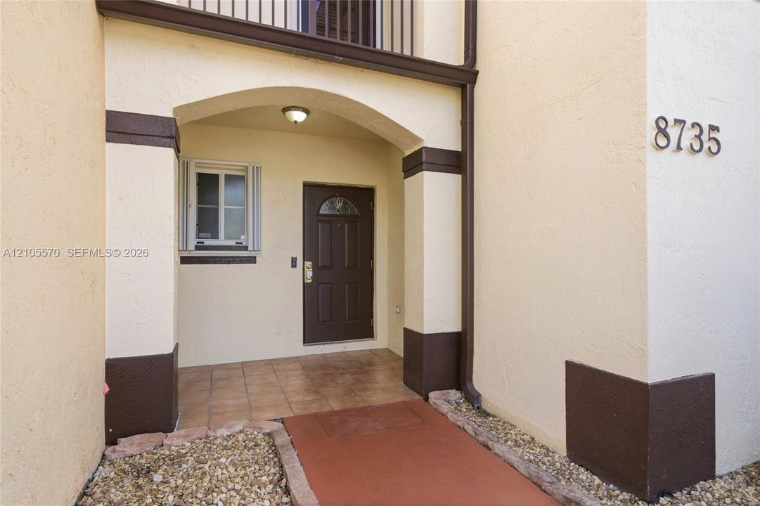 Arched entryway featuring a paneled door with an arched glass insert, exterior wall sconce, and tiled flooring
