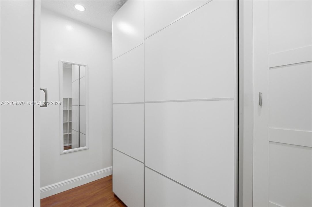 Built-in white cabinetry with horizontal accents, recessed ceiling lighting, wood-finish flooring, and a wall-mounted mirror