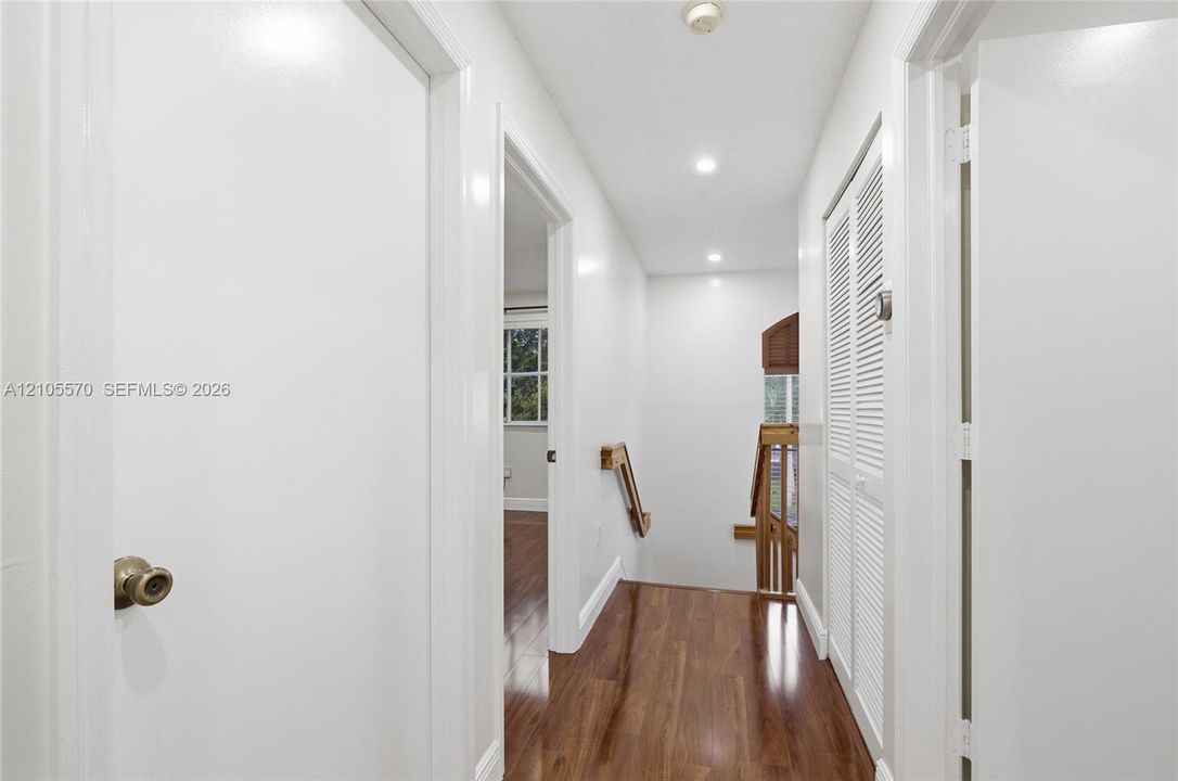 Hallway featuring wood-finish flooring, recessed lighting, and white louvered bifold doors