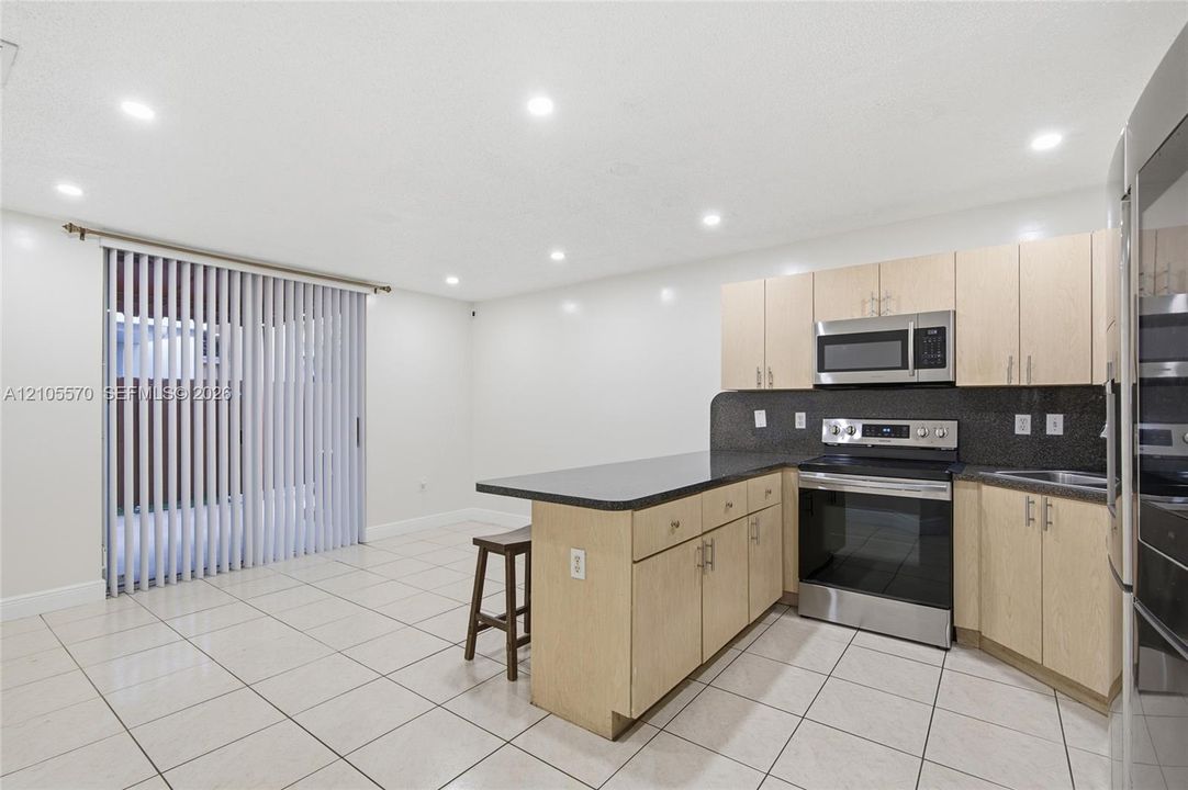 Kitchen featuring light wood-finish cabinetry, dark countertops, stainless steel appliances, and tile flooring