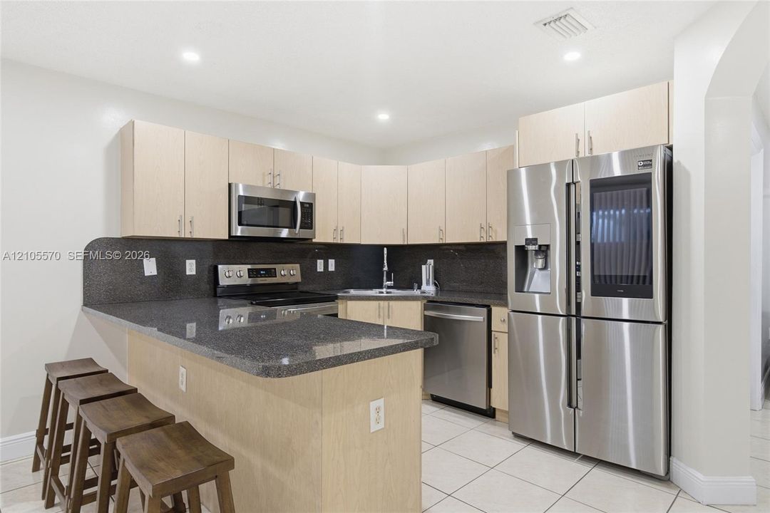 Kitchen featuring light wood-finish cabinetry, dark countertops, full suite of stainless steel appliances, and tiled flooring