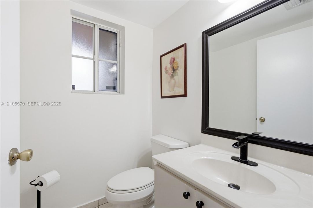 White vanity with a single basin sink, matte black faucet, and framed mirror