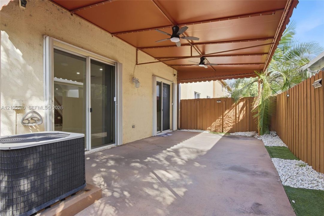 Covered patio with integrated ceiling fans, stucco exterior, sliding glass doors, and a wood privacy fence