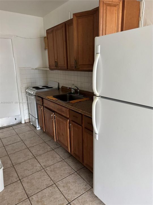 Kitchen featuring medium-toned wood cabinetry, stone-finish countertops, ceramic tile flooring, a white electric range, and a white top-freezer refrigerator