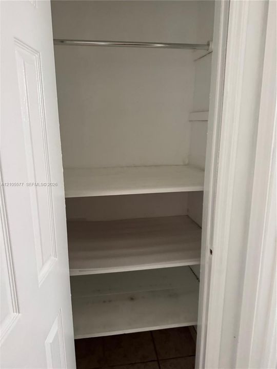 Storage closet featuring white-painted wood shelving and a metal garment rod