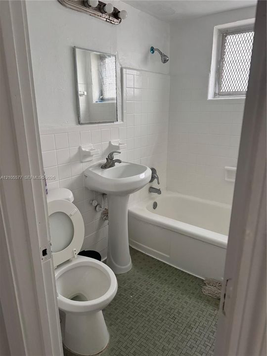 Bathroom featuring a white porcelain pedestal sink, white tiled tub surround, standard bathtub, integrated wall-mounted lighting, and textured flooring