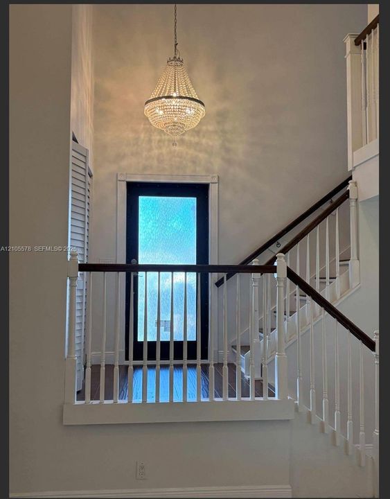Grand entryway featuring a high-reaching ceiling, crystal-accented chandelier, staircase with wood-finish handrail, and a glass-paneled door