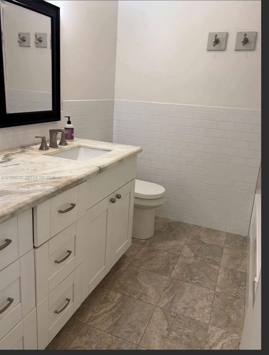 White vanity with a stone countertop, under-mount sink, subway tile wainscoting, and large-format tile flooring