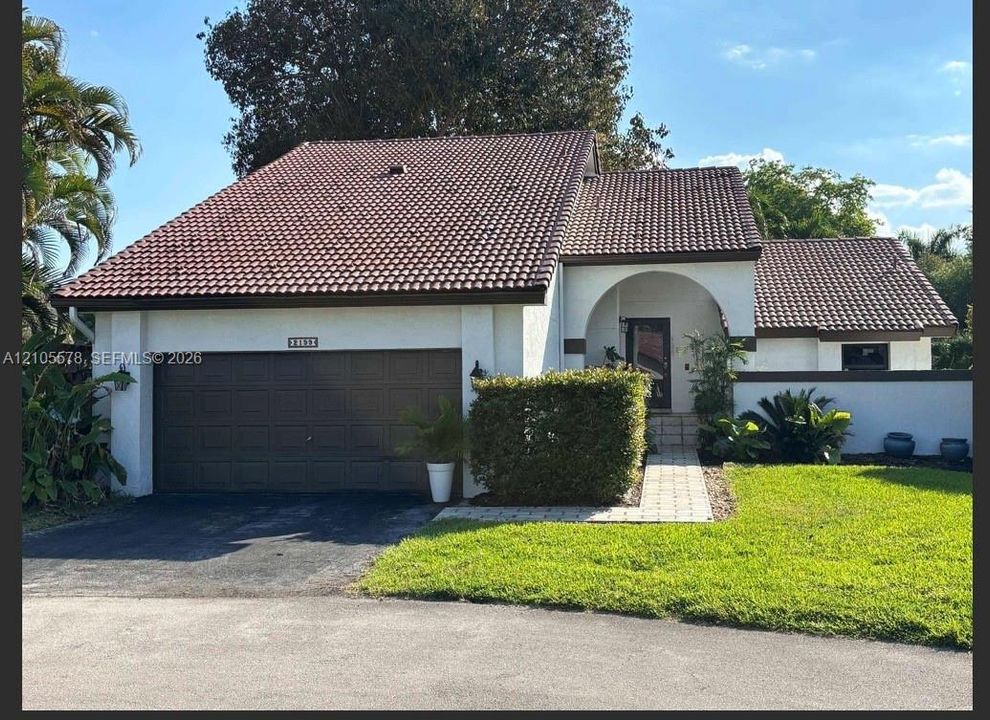 Exterior featuring a concrete tile roof, stucco finish, arched entryway, and attached two-car garage