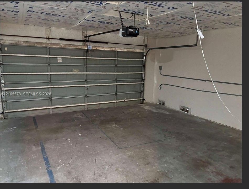 Multi-car garage featuring a sectional overhead door, automated door opener, and exposed interior wall conduit