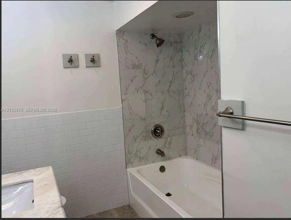Bathtub with stone-finish tile surround, white subway tile wainscoting, integrated countertop vanity, and metal fixtures