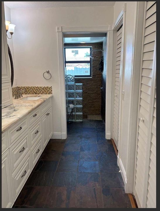 Bathroom featuring a white cabinetry vanity, stone-patterned countertop with a mosaic tile backsplash, slate-finish floor tile, and a textured stone wall in the shower area