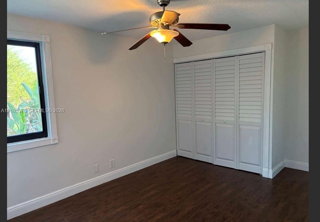 Interior room featuring wood-finish flooring, a multi-pane window with white trim, a ceiling fan with integrated lighting, and a bi-fold louvered closet door