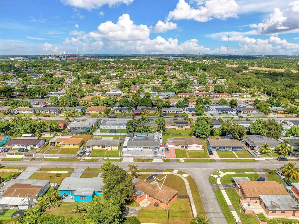 Aerial perspective of a residential property featuring a composition shingle roof, paved driveway, and established landscaping