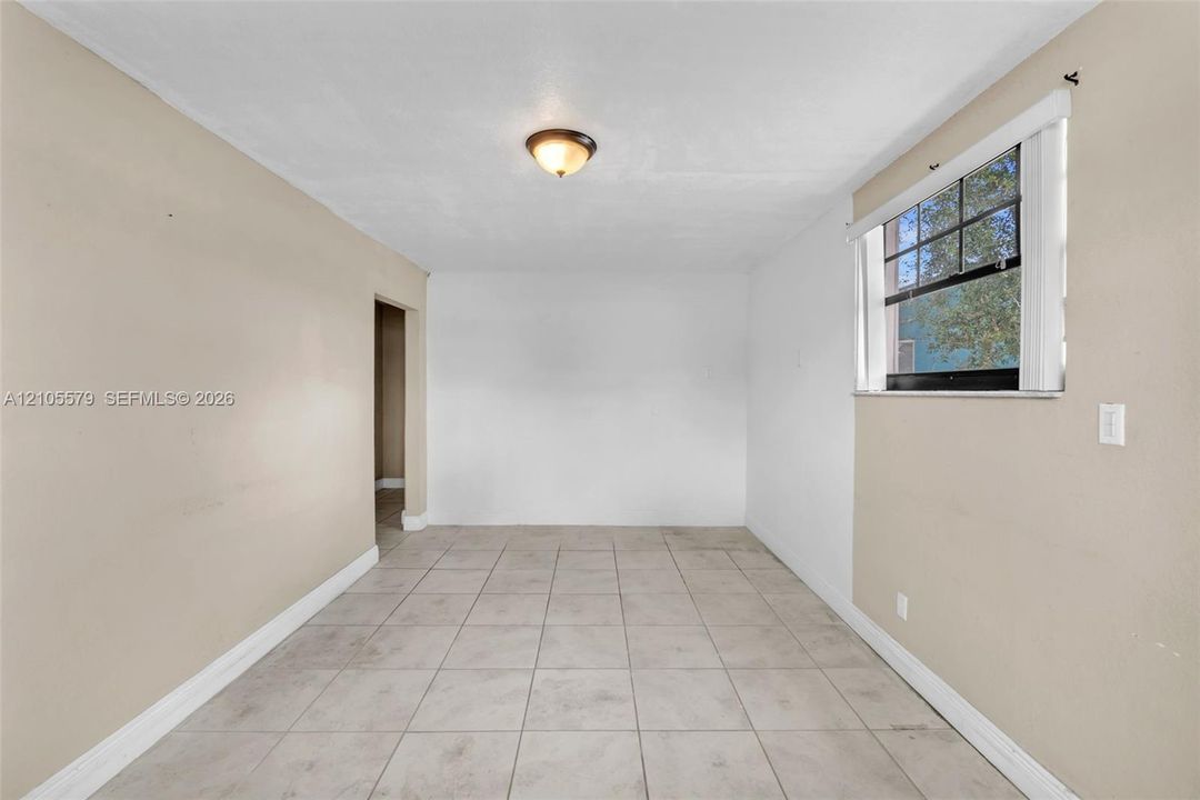 Neutral-toned interior space featuring light-colored tile flooring, smooth walls, a single-pane window with dark muntins, and a flush-mount ceiling light fixture