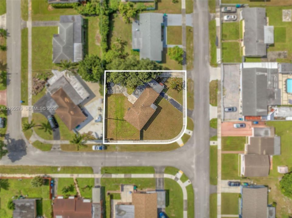 Corner lot featuring a multi-pitched shingled roof, paved driveway, and established trees within the fenced perimeter
