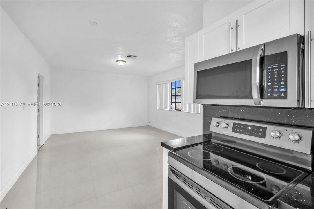 Kitchen featuring white shaker-style cabinetry, a stainless steel microwave, and a glass-top electric range with a dark solid-surface countertop