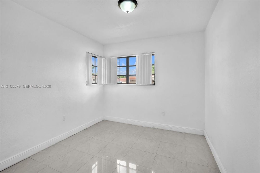 Neutral interior space featuring polished tile flooring, smooth white walls, corner-positioned multi-pane windows, and a flush-mount ceiling fixture