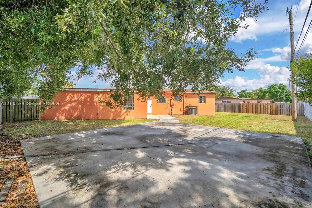 Stucco exterior featuring a concrete driveway, fenced perimeter, and mature canopy trees