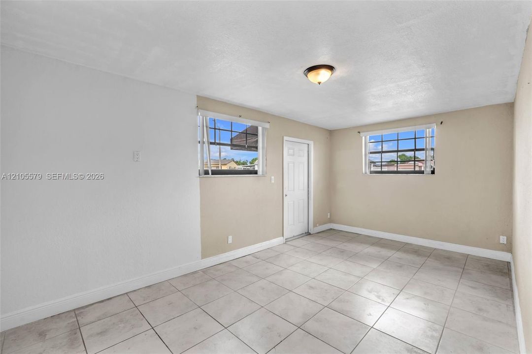 Neutral-toned interior space featuring large-format ceramic tile flooring, two multi-pane windows with hardware, and a single-panel interior door