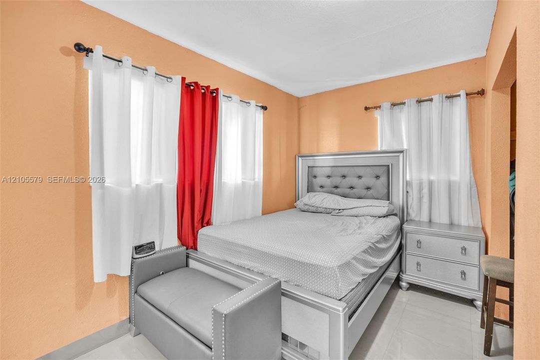 Bedroom with dual-aspect windows, white-finished rod hardware, and light-colored tile flooring