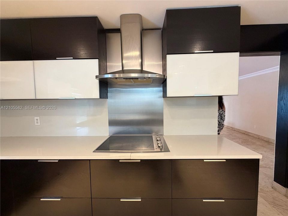 Integrated cooktop with stainless steel range hood, white countertop, and two-tone cabinetry