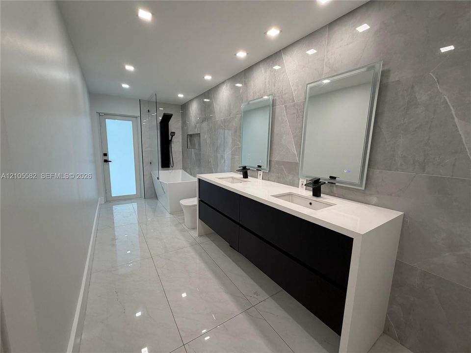 Dual vanity with waterfall countertop, matte black fixtures, integrated sinks, and mirrored medicine cabinets