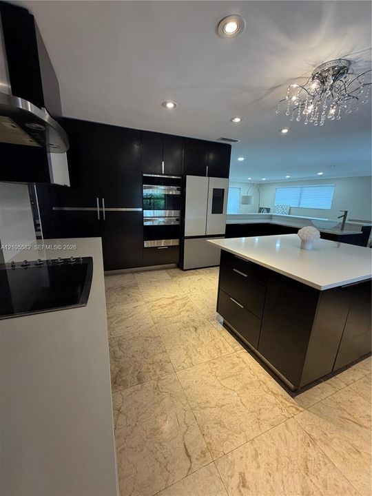Contemporary kitchen featuring sleek dark cabinetry, integrated stainless steel appliances, a central island with a white countertop, and recessed lighting