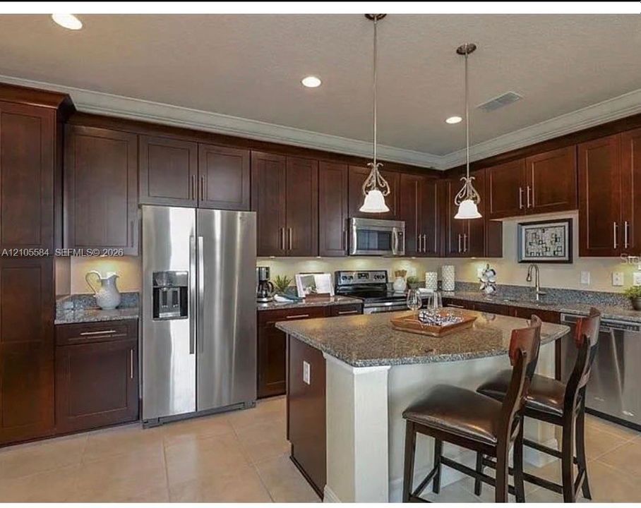 Kitchen featuring dark wood cabinetry, stone countertops, stainless steel appliances, a central island with bar seating, and pendant lighting