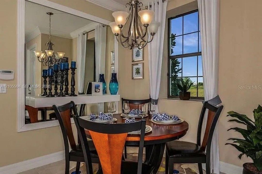 Dining area featuring crown molding, a large wall-mounted mirror with decorative trim, a multi-arm chandelier, and a multi-pane window