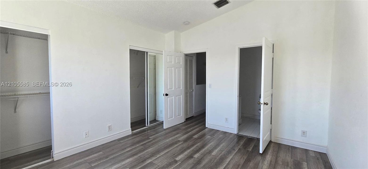 Room featuring wood-finish flooring, vaulted ceiling, mirror-panel sliding closet door, and traditional six-panel interior doors