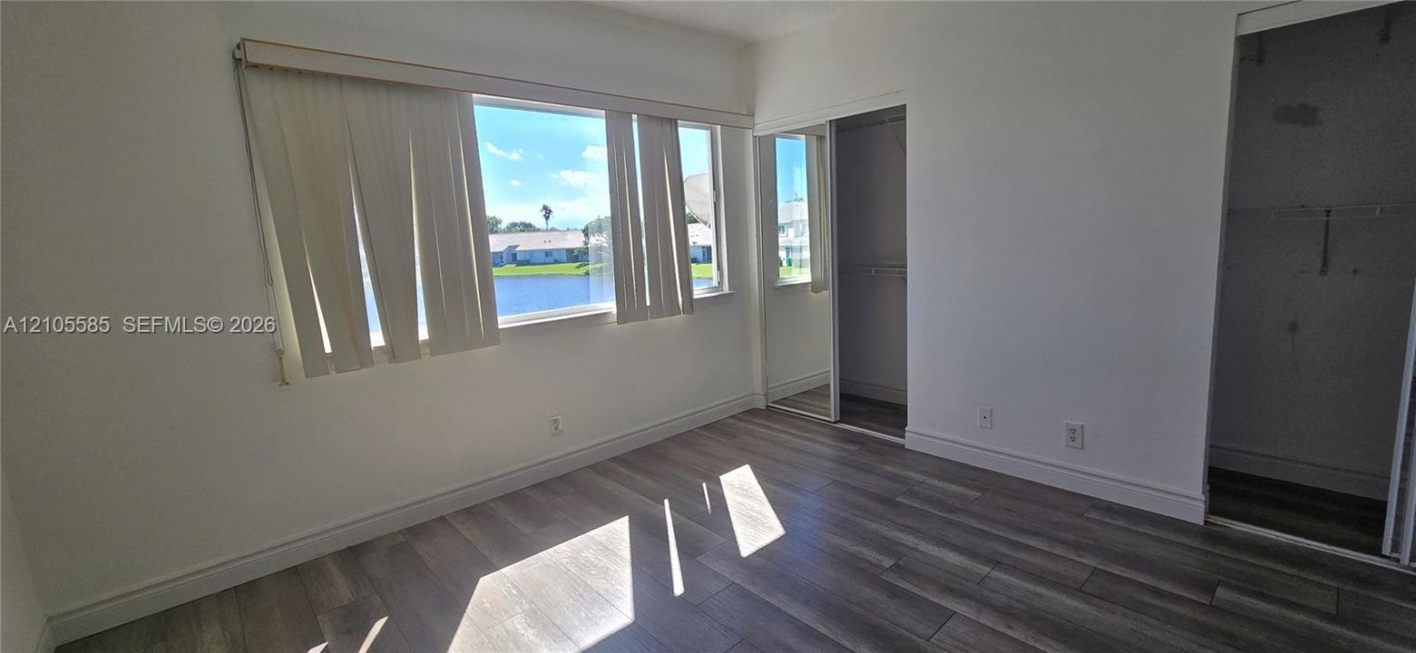 Wood-finish flooring, large window with vertical blinds, and a built-in closet with mirrored sliding doors