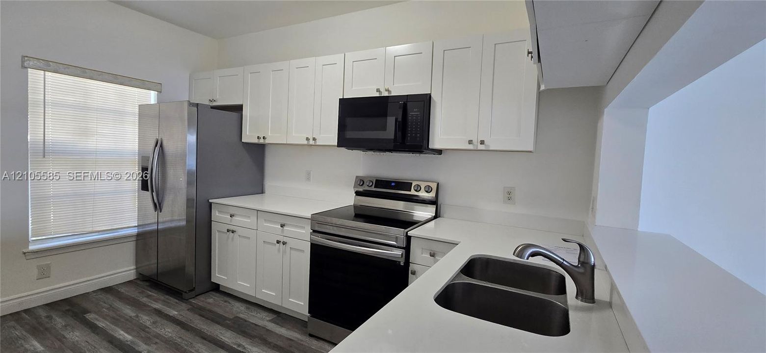Kitchen featuring white shaker-style cabinetry, solid-surface countertops, wood-finish flooring, stainless steel appliances, and an undermount dual-basin sink with a pull-down faucet