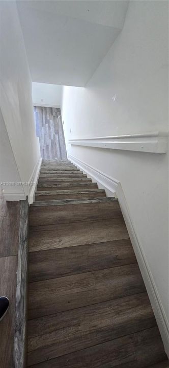Staircase featuring wood-finish treads and a wall-mounted handrail