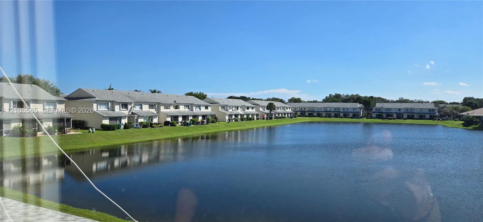 Waterfront location featuring a large retention pond, manicured lawn, and multi-unit residential structures with light-colored siding and shingled roofs